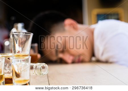Hangover sleeping man behind the empty glasses and bottle on table