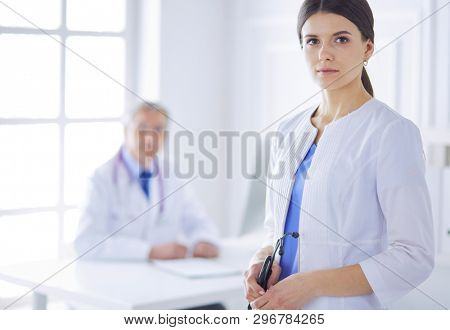 A doctor looking at the camera with her male colleage in the back of the conference room in hospital