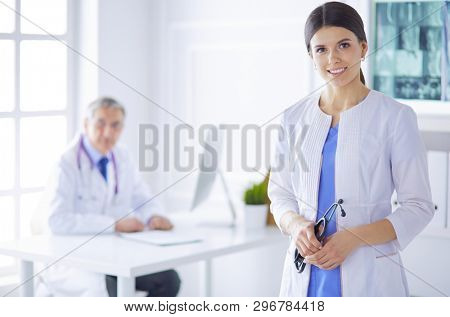 A doctor looking at the camera with her male colleage in the back of the conference room in hospital