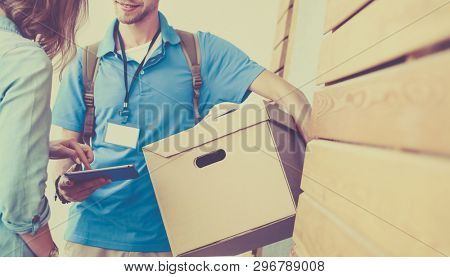 Smiling delivery man in blue uniform delivering parcel box to recipient - courier service concept