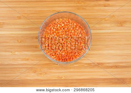 Top View Of Glass With Raw Split Red Lentil Seeds On A Bamboo Wooden Cutting Board
