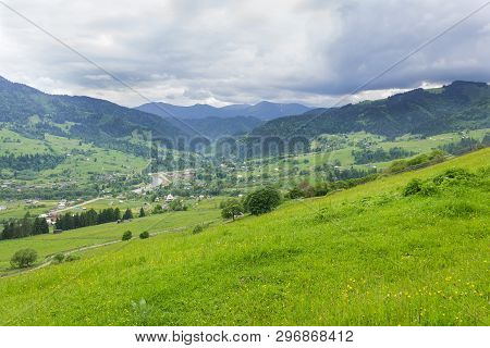 Mountain Village In Valley With Pastures And Fenced Hayfields On Slope On A Foreground Against Storm