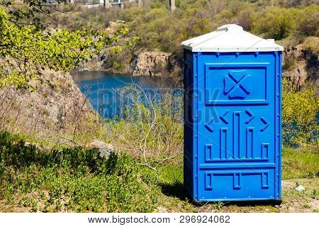 Blue Cabine Of Bio Toilet In A Mountain Park On A River Background At Sunny Summer Day.