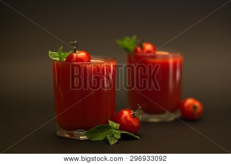 Two glasses of tomato juice with cherry tomatoes and mint with a black background