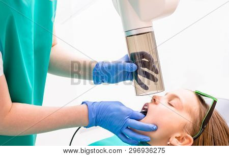 Radiographer taking teeth radiography to a girl using digital x-ray machine in pediatric dental clinic. Doctor pointing X-ray unit while holding electronic sensor in child's  mouth performing scanning