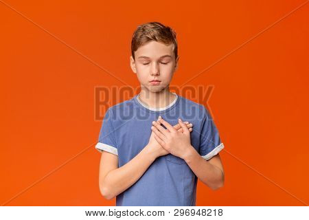 Touched Sensitive Teenage Boy Pressing Hands To Chest Being Grateful, Orange Studio Background
