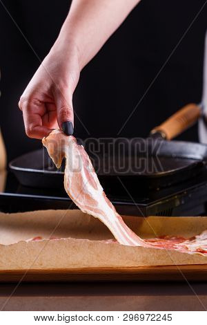 Young Woman In A Gray Apron Fries Bacon