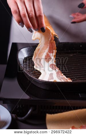 Young Woman In A Gray Apron Fries Bacon
