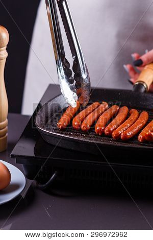Young Woman In A Gray Apron Fries Sausages