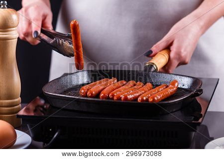 Young Woman In A Gray Apron Fries Sausages