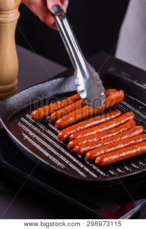 Young Woman In A Gray Apron Fries Sausages