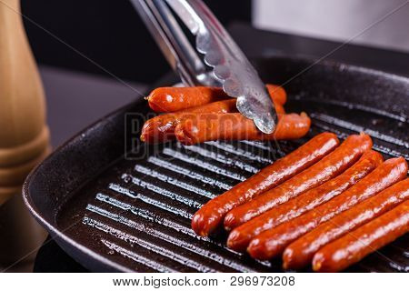 Young Woman In A Gray Apron Fries Sausages
