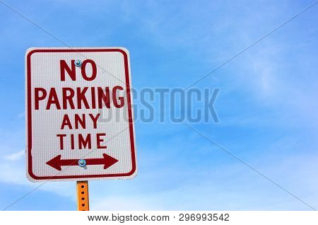 Road Side Sign Communicating Not To Park In The Space To The Left Or Right Against A Blue Sky
