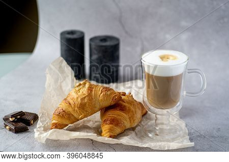 On A Gray Table There Is A Glass Cup With Hot Latte Coffee And Next To It.two Croissants Lie On A Gr