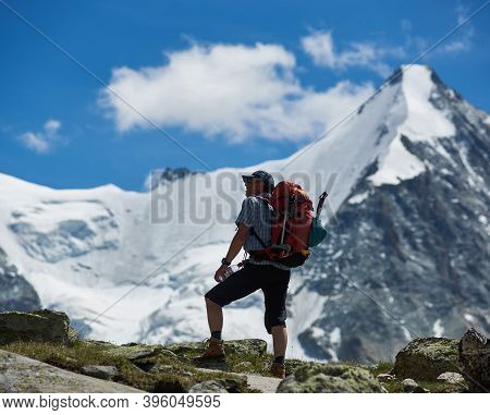 Zinal, Switzerland - July 19, 2019: Man Traveler With Backpack Holding Bottle Of Water And Enjoying 