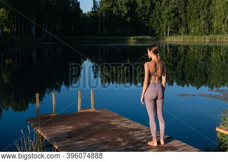 Young Woman Relaxing By The Lake At Sunset, Harms Outstretched. Doing Youga In The Morning At Forest