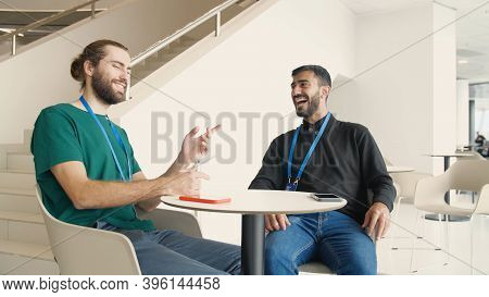 Young Workers Talk During Their Lunch Break In Office. Media. Two Colleagues With Badges Are Talking