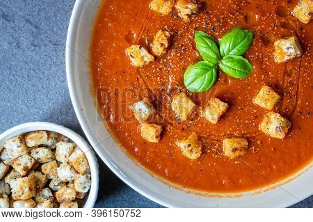 A Bowl Of Fresh Homemade Organic Tomato And Basil Soup With A Side Ramekin Of Croutons And A Garnish