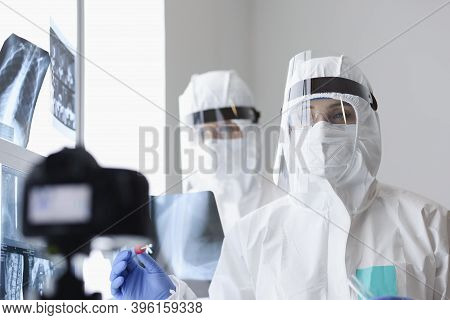 Doctors In Protective Screens And Anti-plague Suits Looking Into Camera In X-ray Room. Blogging Duri