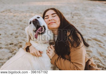 Beautiful Young Woman Hugging With Her Golden Retreiver Dog On The Beach At Autumn Warm Day