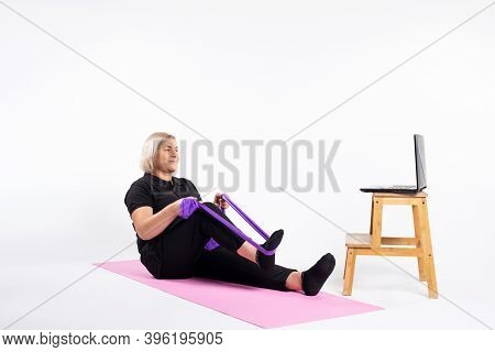 Senior Woman Sitting, Doing Exercises With An Elastic Band. Online Training.