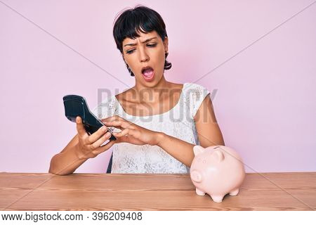 Beautiful brunettte woman caculating money savings in shock face, looking skeptical and sarcastic, surprised with open mouth 