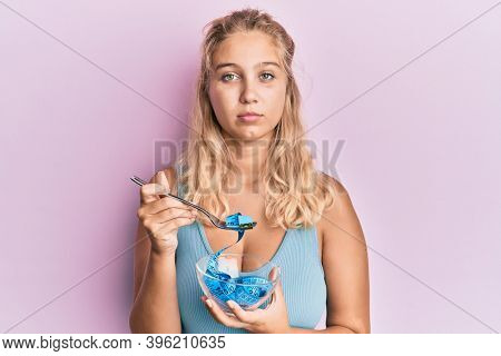 Young blonde girl eating measure meter doing diet for weight loss relaxed with serious expression on face. simple and natural looking at the camera. 