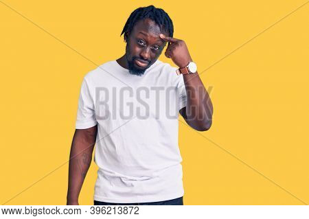 Young african american man with braids wearing casual white tshirt pointing unhappy to pimple on forehead, ugly infection of blackhead. acne and skin problem 