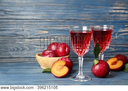 Delicious Plum Liquor And Ripe Fruits On Blue Wooden Table. Homemade Strong Alcoholic Beverage