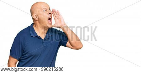 Middle age bald man wearing casual clothes shouting and screaming loud to side with hand on mouth. communication concept. 