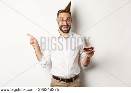 Holidays And Celebration. Happy Man Enjoying Birthday Party, Holding Bday Cake And Pointing Finger L