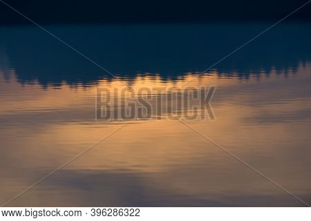 A Warm Orange Glowing Sunset Behind A Line Of Conifer Trees Is Reflected And Displayed Upside Down I
