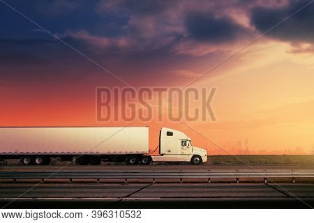 White freight truck driving on freeway road under red sunset sky.