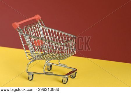 Empty Shopping Cart On Colorful Yellow And Brown Background. Online Shopping Or E-commmerce Concept.