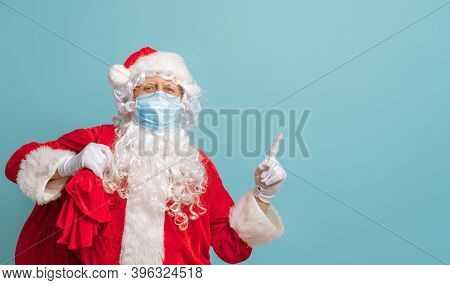 Merry Christmas and Happy Holidays! Santa Claus in face mask on bright color background. Covid-2019