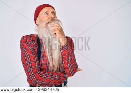 Old senior man with grey hair and long beard wearing hipster look with wool cap with hand on chin thinking about question, pensive expression. smiling and thoughtful face. doubt concept. 