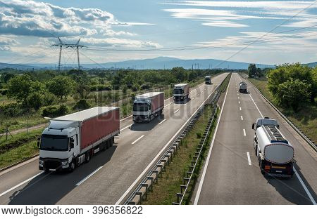 Four Lanes Highway Transit With Transportation Trucks And Tank Truks On A Bright Blue Day. Highway T