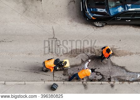 Road Workers In Orange Vests Repair The Road. Pit Removal And Patching. View From Above. Works Of Re