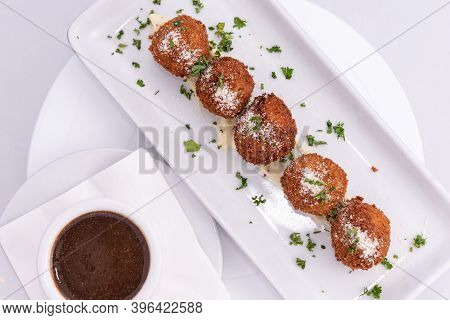 Overhead View Of Parmesan Topped Risotto Arancinis Italian Meatballs Lined Up On A Rectangular Plate