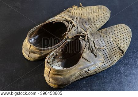 Old Torn Yellow Summer Shoes On A Black Background. A Pair Of Men's Heavily Worn Leather Shoes.
