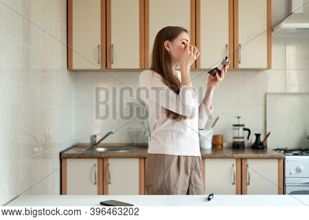 Young Woman Doing Make Up In Kitchen And Looking In Mirror. Hurrying To Work.