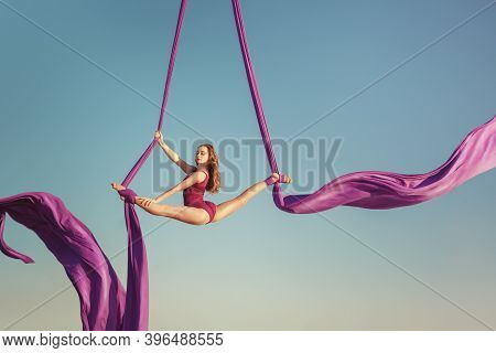 The Gymnast Artist Performs High In The Sky. She Flies On The Canvas Showing Tricks.