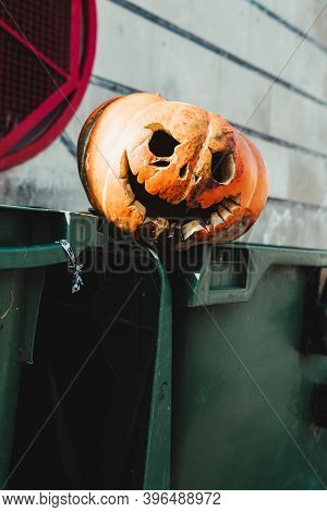 Rotten Carved Pumpkin Over Garbage Bins. She Has A Malefic Smile. Smiling Jack O Lantern. End Of Hal