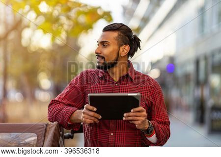 Smiling young man using tablet outdoors at urban setting
