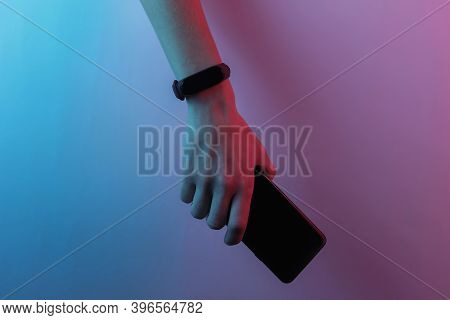 Female Hand With Smart Bracelet And Smartphone. Modern Gadgets. Creative Pop Art Pink Blue Neon Colo