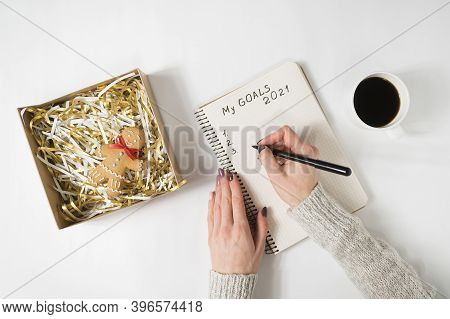 Female Hands Writing My Goals 2021 In A Notebook. Mug Of Coffee And Gingerbread Man, Top View.