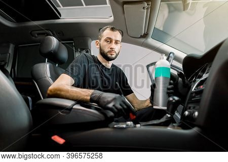 Young Concentrated Male Car Service Worker Cleaning Dust From Interior Of Luxury Car, Using Special 