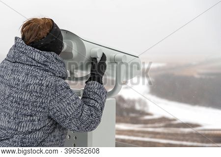 A Woman Looks Through A Binoscope At A Winter Landscape. Copy Space.
