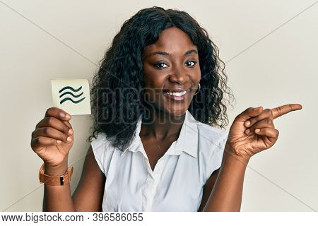 Beautiful black woman holding paper with aquarius zodiac sign smiling happy and positive, thumb up doing excellent and approval sign 