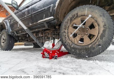 Change Tire Witn Floor Rolling Hydraulic Jack And Wrench. Winter Background.